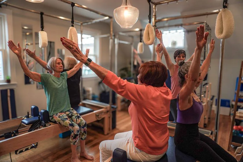 A group reformer Pilates session reaching overhead at the towers